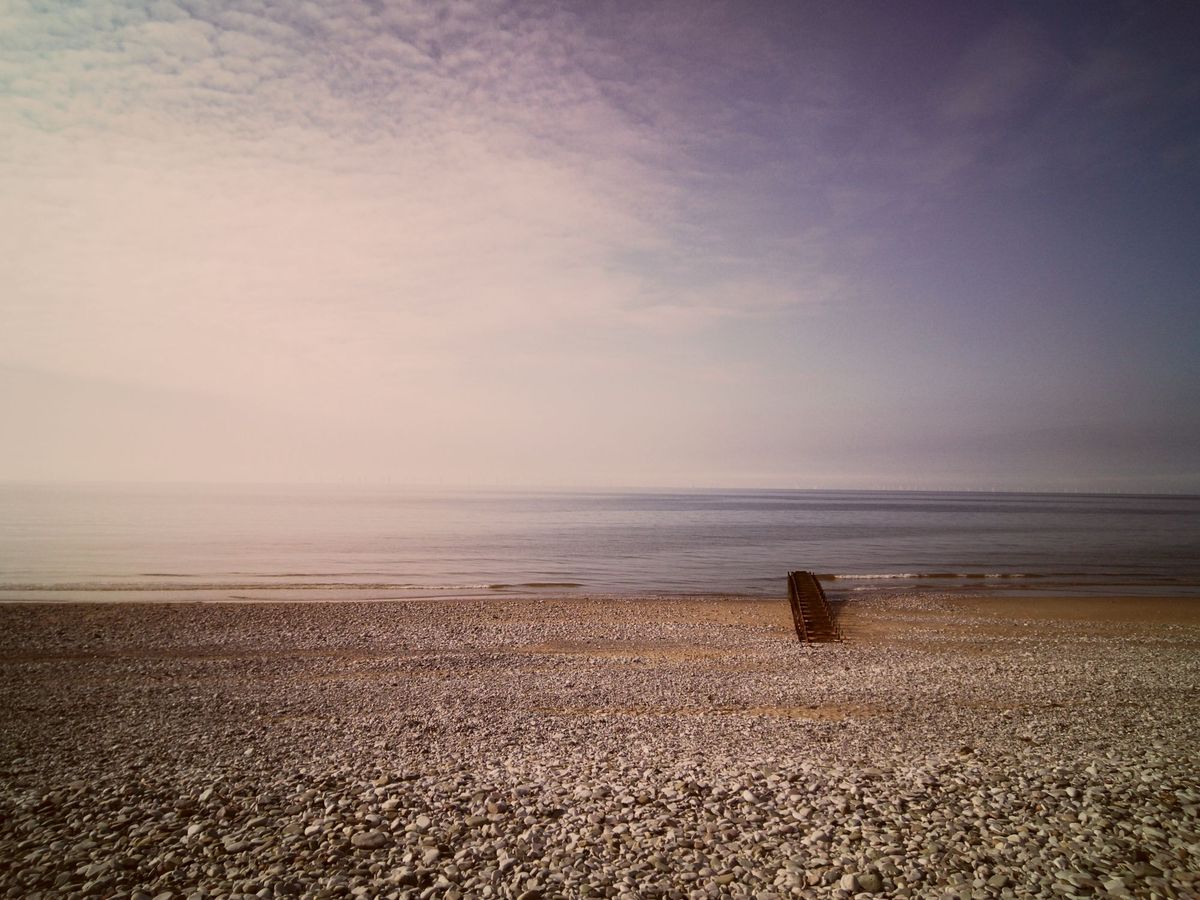 Pebble beach and a calm, hazy sea at Pensarn, Wales